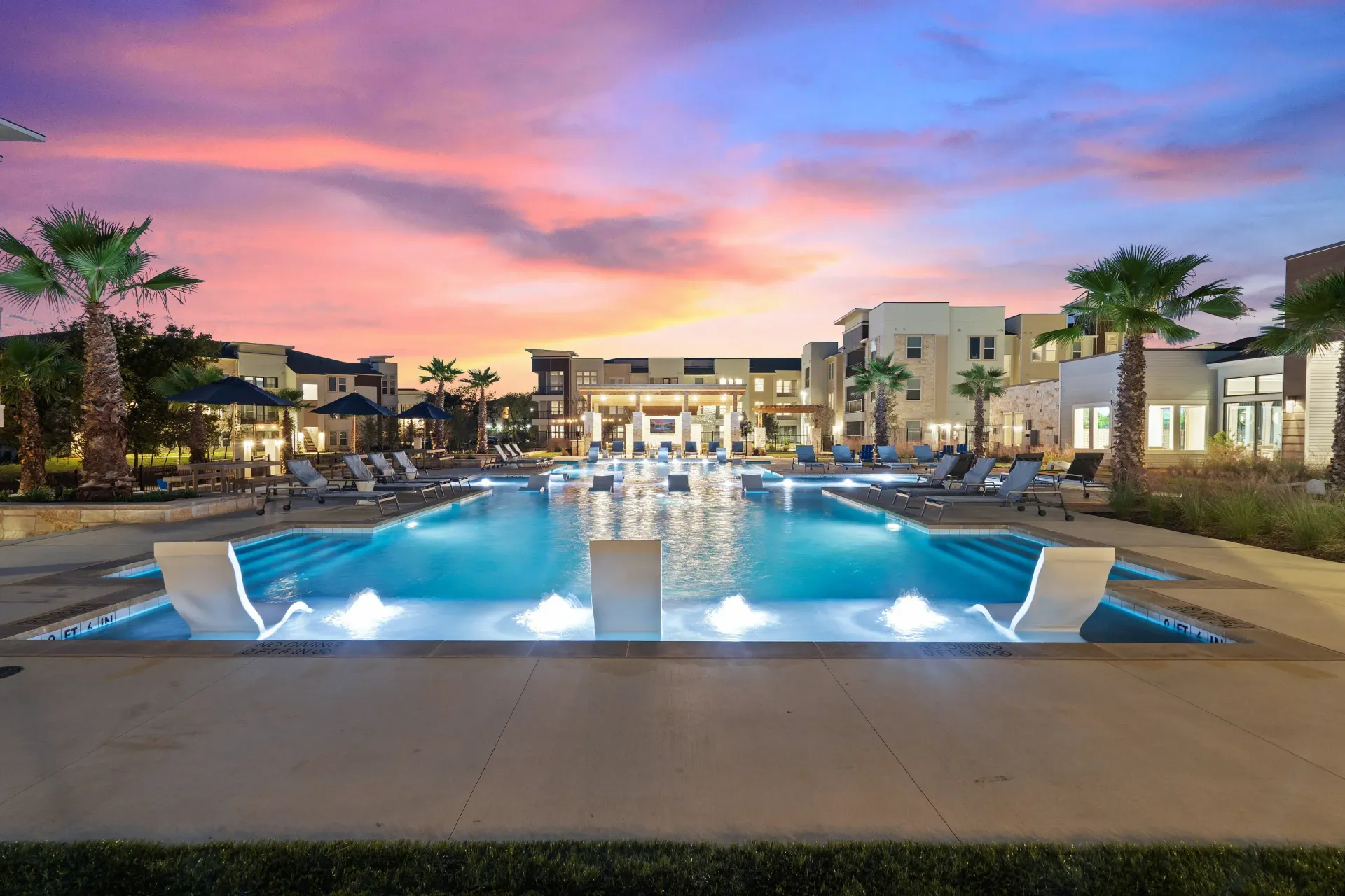 Outdoor resort-style pool at a multifamily property with lounge chairs and palm trees at sunset.