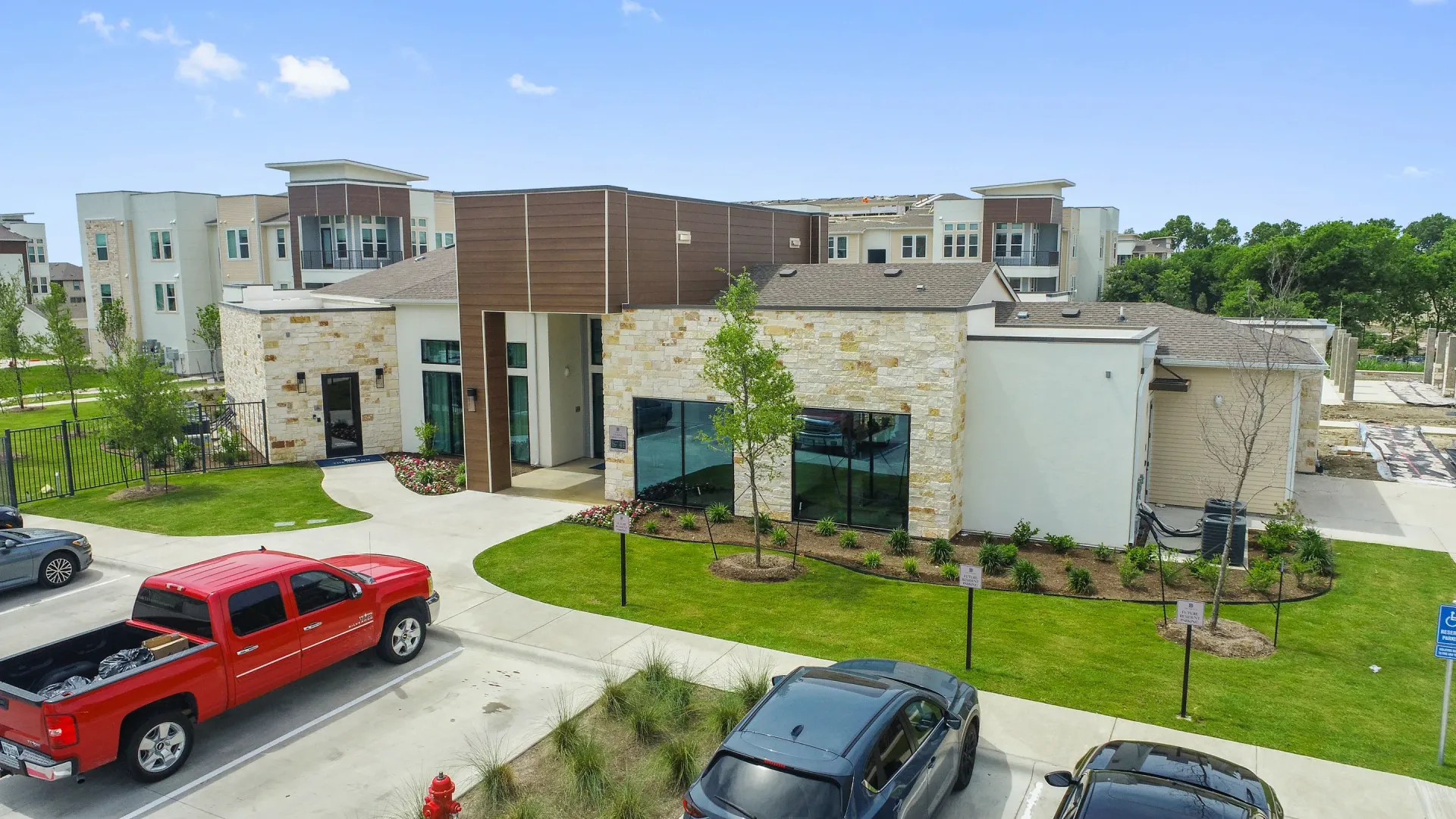 Exterior view of a modern multifamily community with stone facade, landscaping, and parked cars.