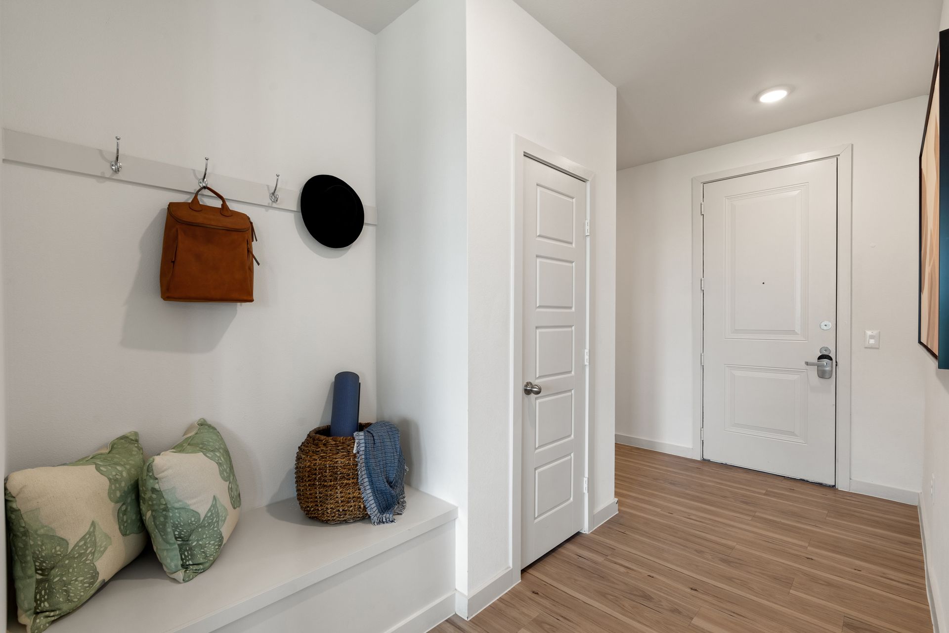 White entry hall with a bench, coat hooks, a brown bag, and hats by the door.