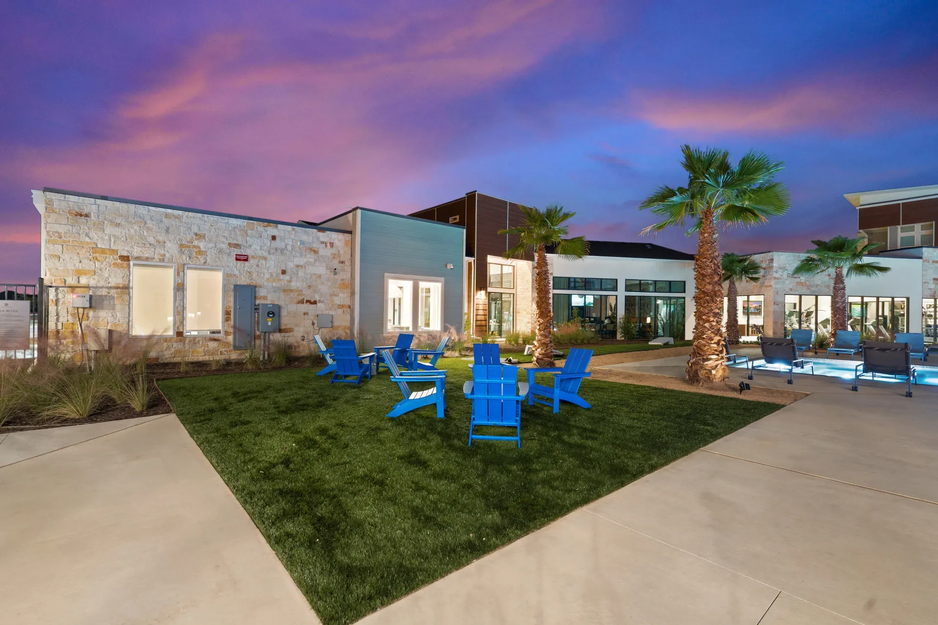 Exterior community pool area with blue lounge chairs and palm trees at dusk.