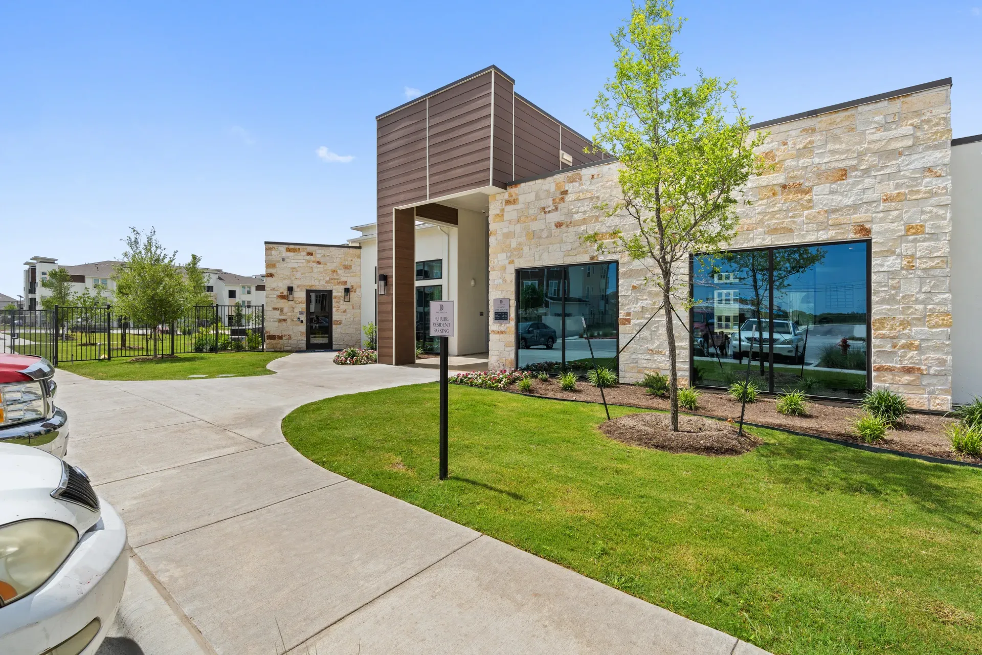 Exterior view of a modern apartment community entrance with stone walls, glass windows, and landscaping.