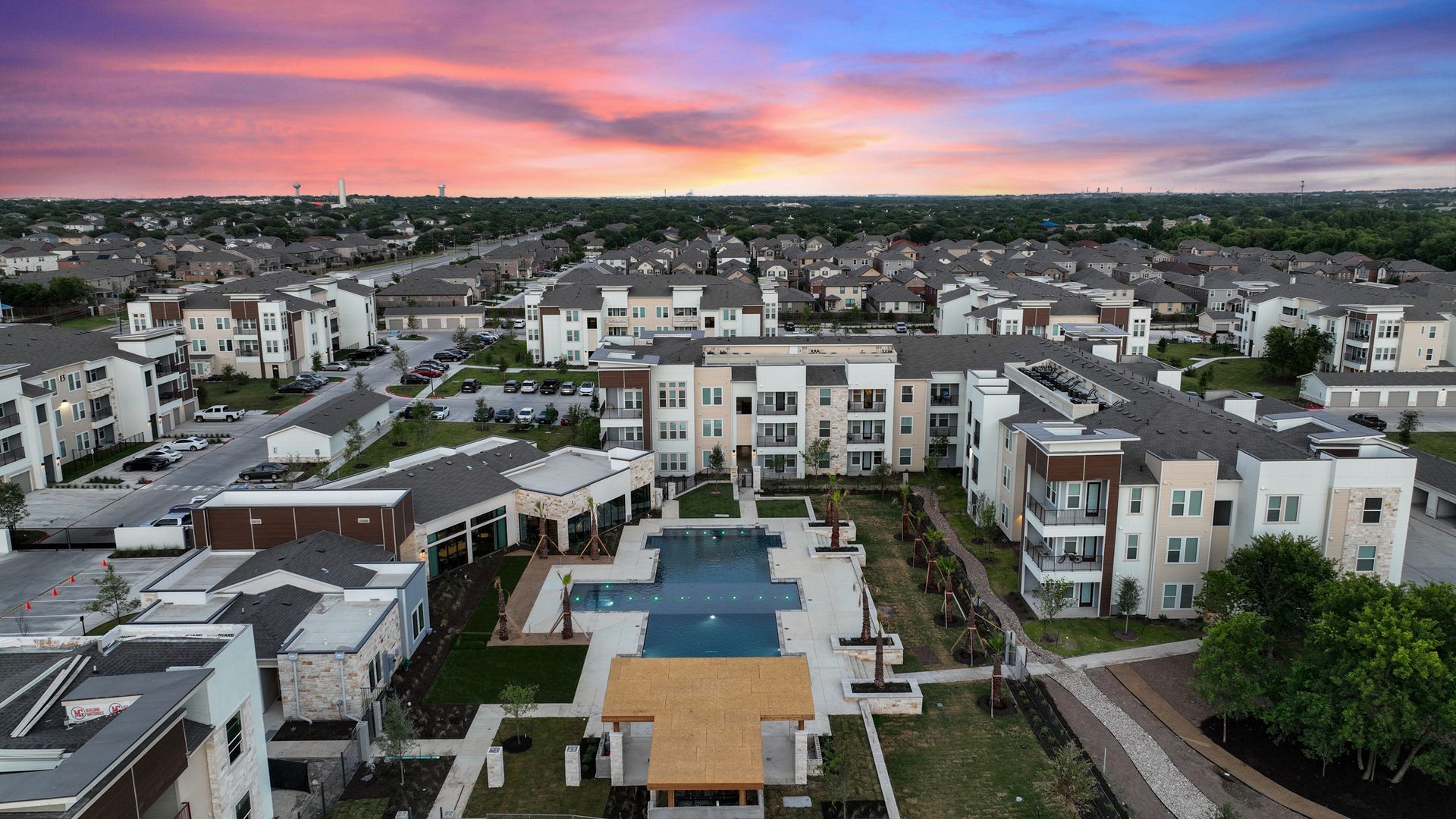 Drone aerial view of a large apartment community with a central pool and surrounding buildings.