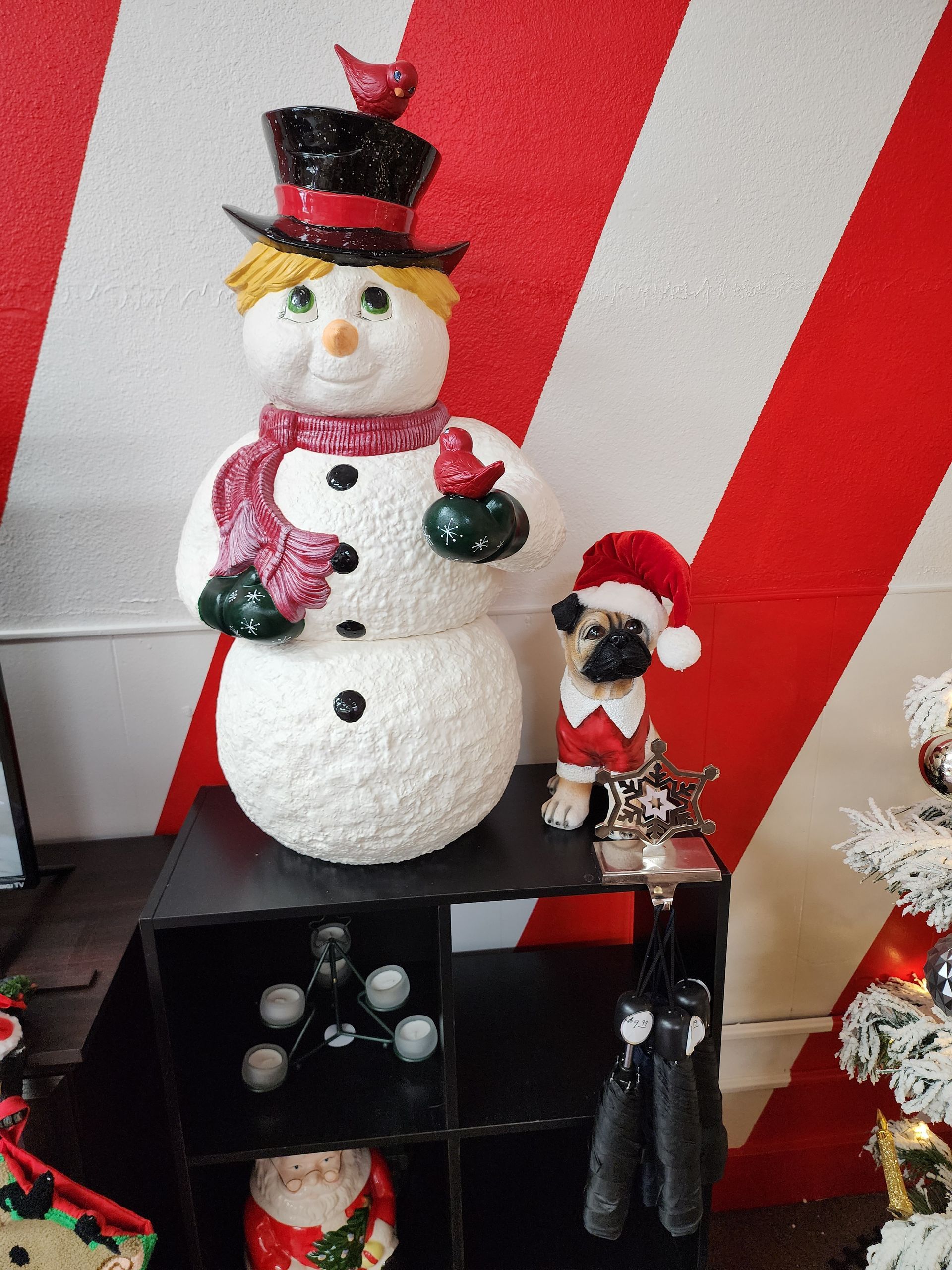 A snowman is sitting on a shelf next to a dog wearing a santa hat.