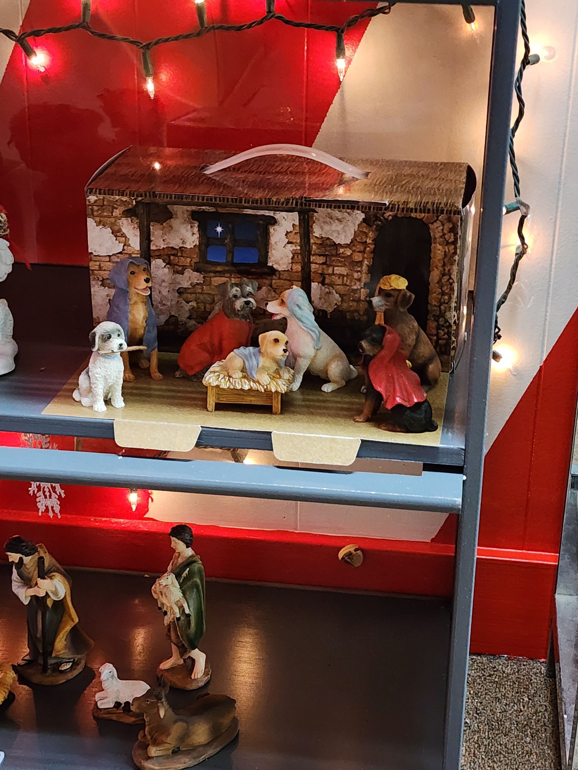 A nativity scene is displayed on a shelf with christmas lights.