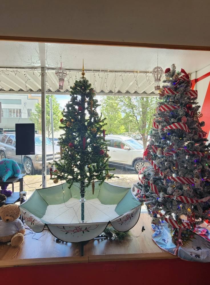 A christmas tree is sitting in an umbrella in front of a window.