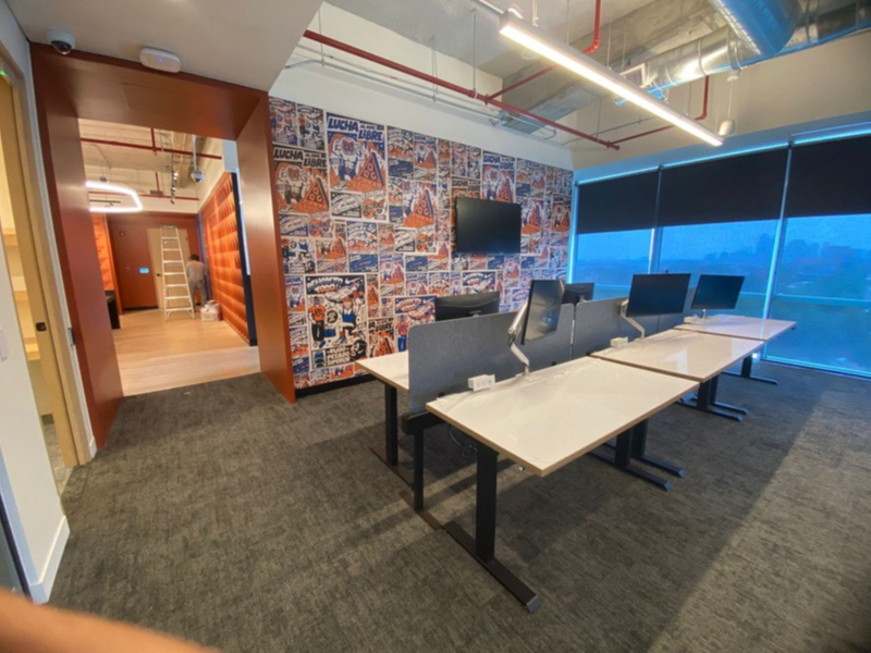 Modern office meeting room with desks, chairs, wall art, and large windows overlooking a blue-lit view