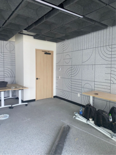Empty office room with patterned walls, gray carpet, wood door, and desks along the sides.