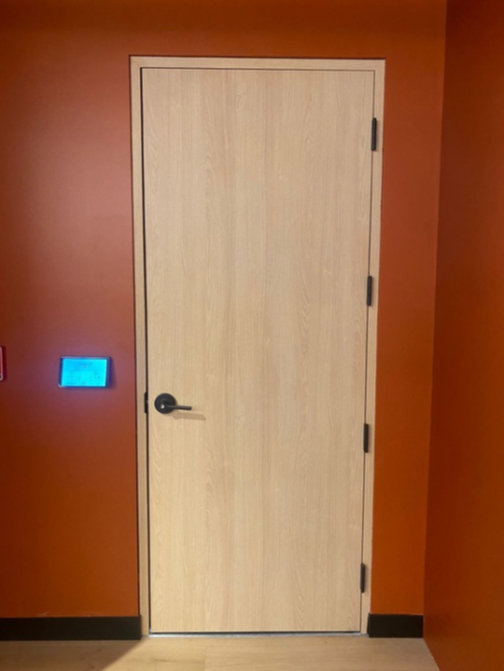 Light wood door with black handle in an orange wall, beside a blue-lit wall panel.