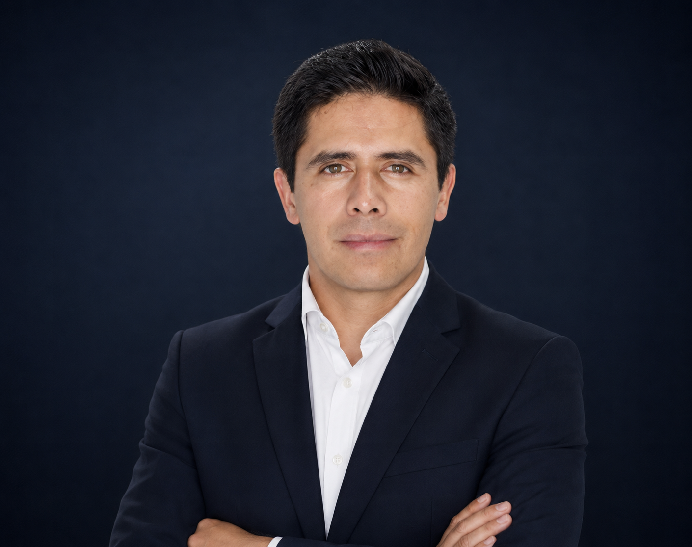 Studio portrait of a man in a dark suit and white shirt with arms crossed against a dark background