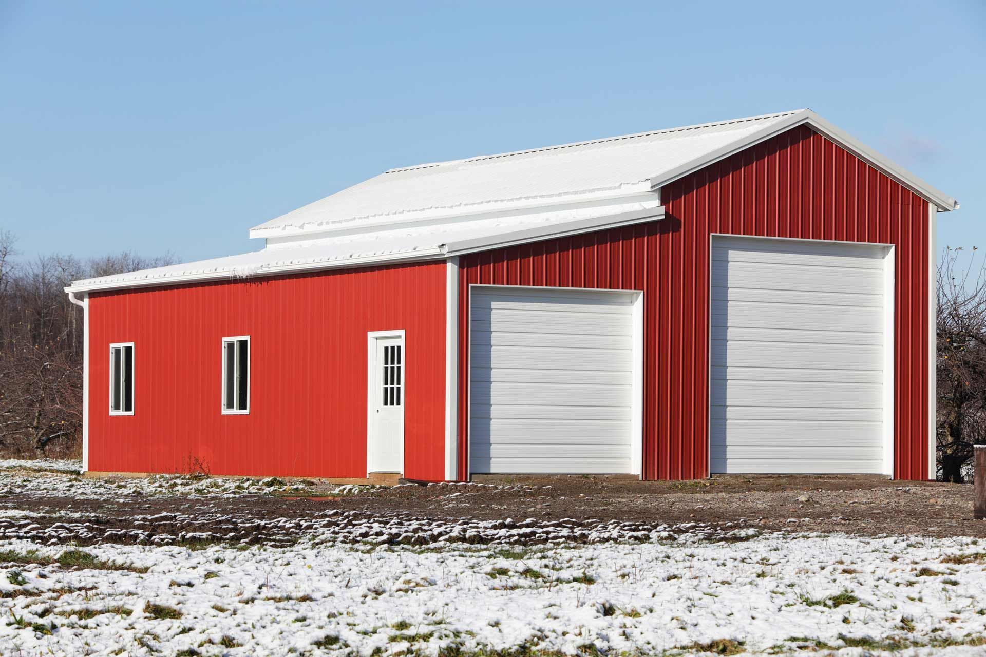 A red barn with two white garage doors in a snowy field