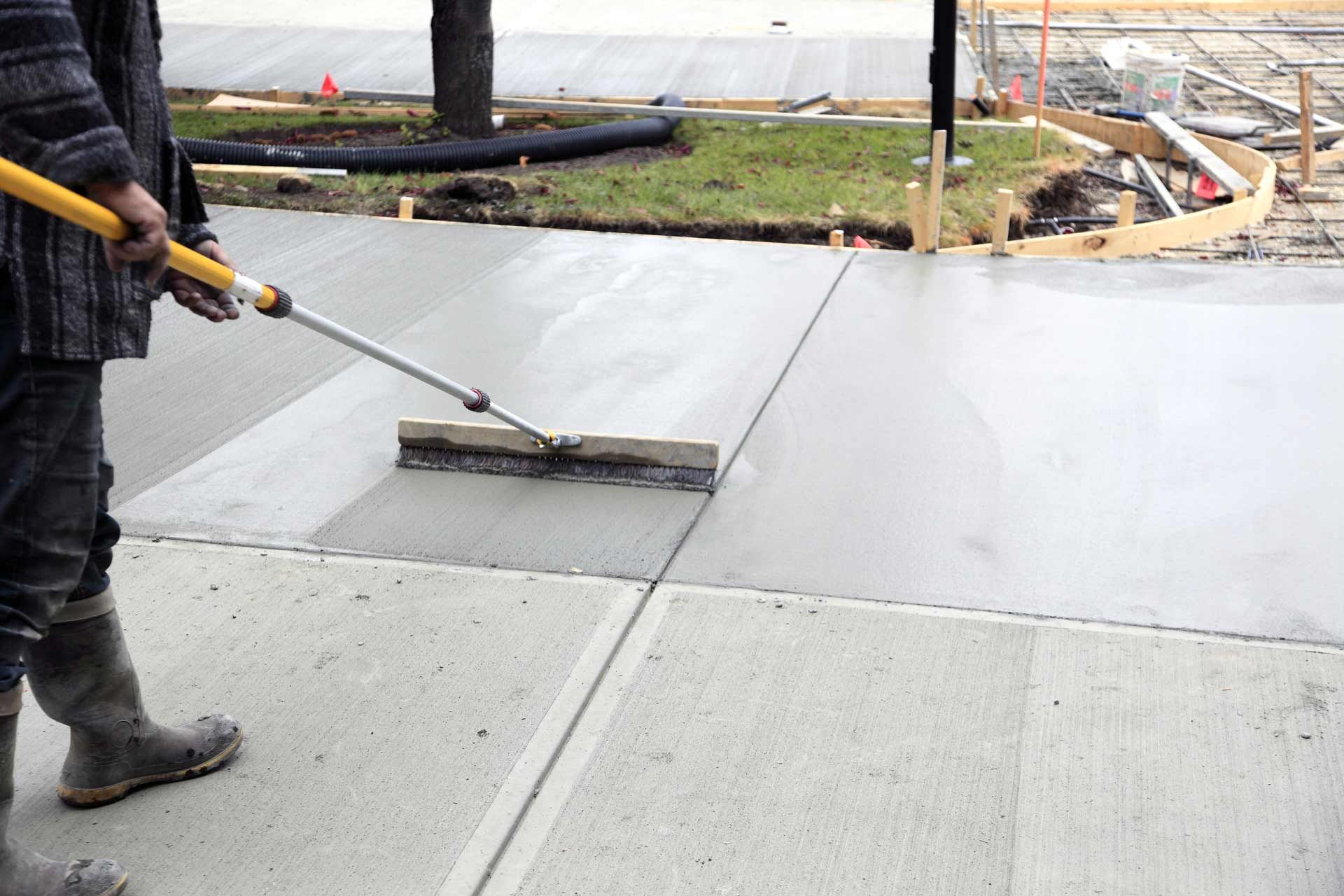 A man is using a broom to spread concrete on a sidewalk