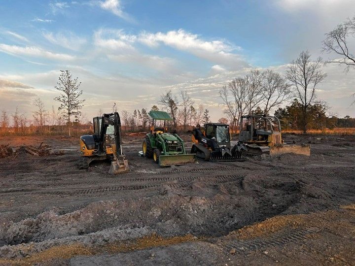 A group of construction vehicles are parked in a dirt field.