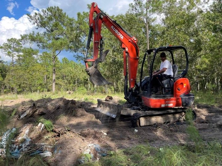 A man is driving a red excavator in a field.