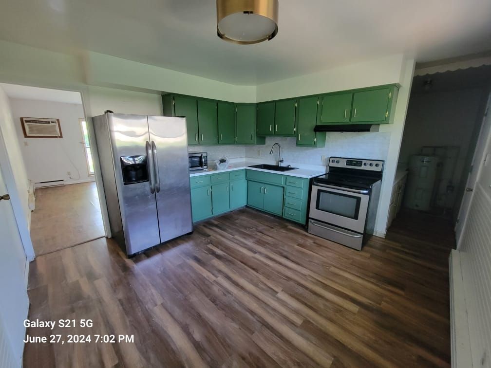 A kitchen with green cabinets , a stainless steel refrigerator , a stove , and a sink.