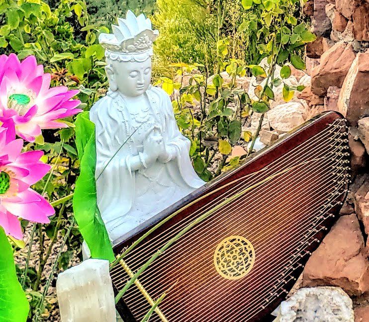 A statue of a woman is sitting next to a harp in a garden.