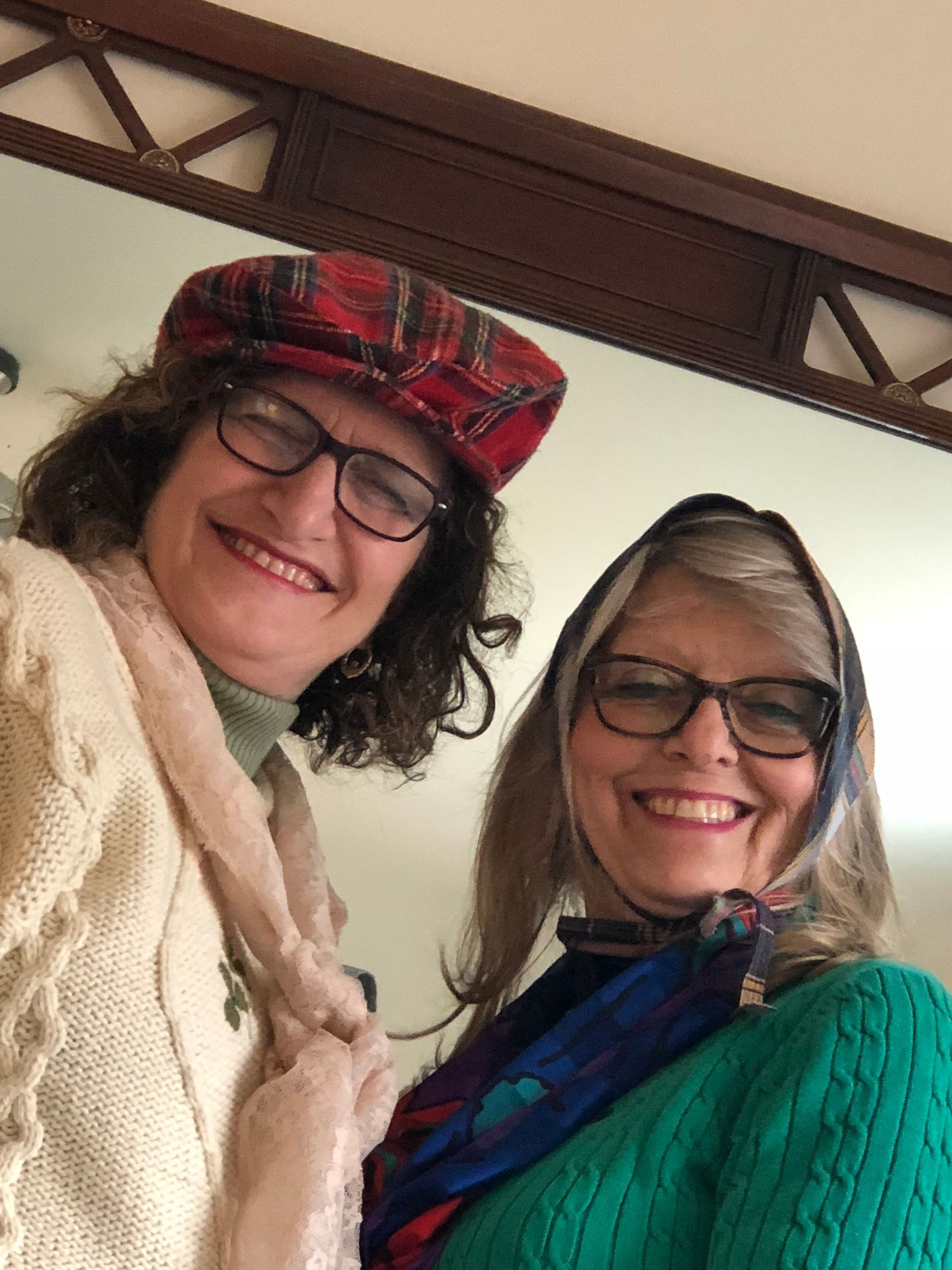 Two women wearing glasses and scarves are smiling for a picture