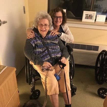 A woman is sitting next to an older woman in a wheelchair.