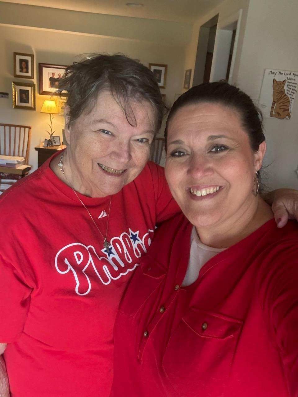 Two women are posing for a picture and one of them is wearing a phillies shirt.