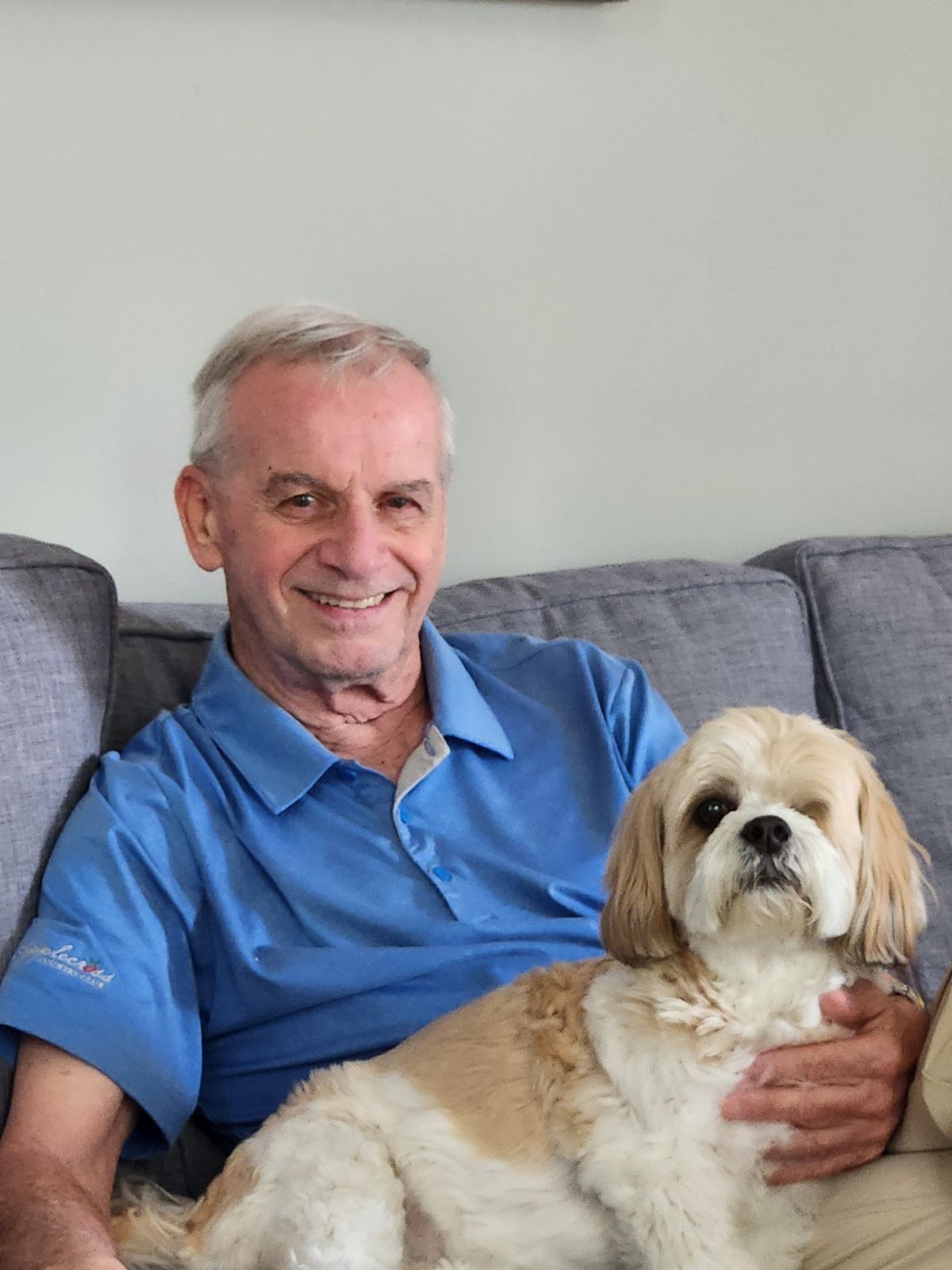 A man is sitting on a couch holding a small dog.