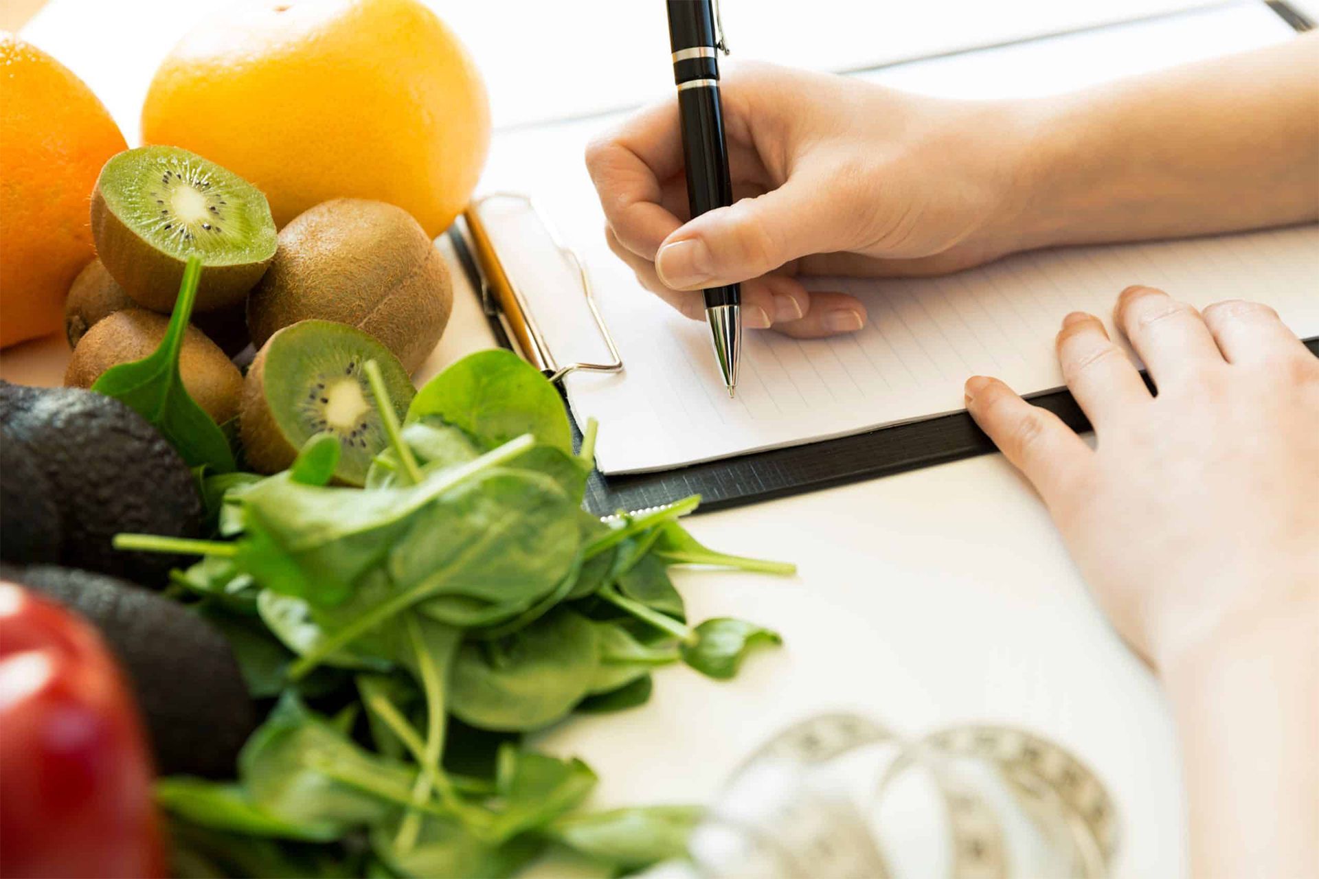 A person is writing on a clipboard with fruits and vegetables in the background