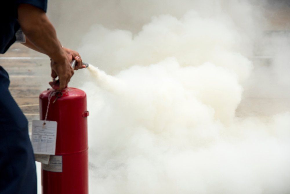 A Man Is Using a Fire Extinguisher to Put out A Fire — Fire Protection Services in Mullumbimby, NSW