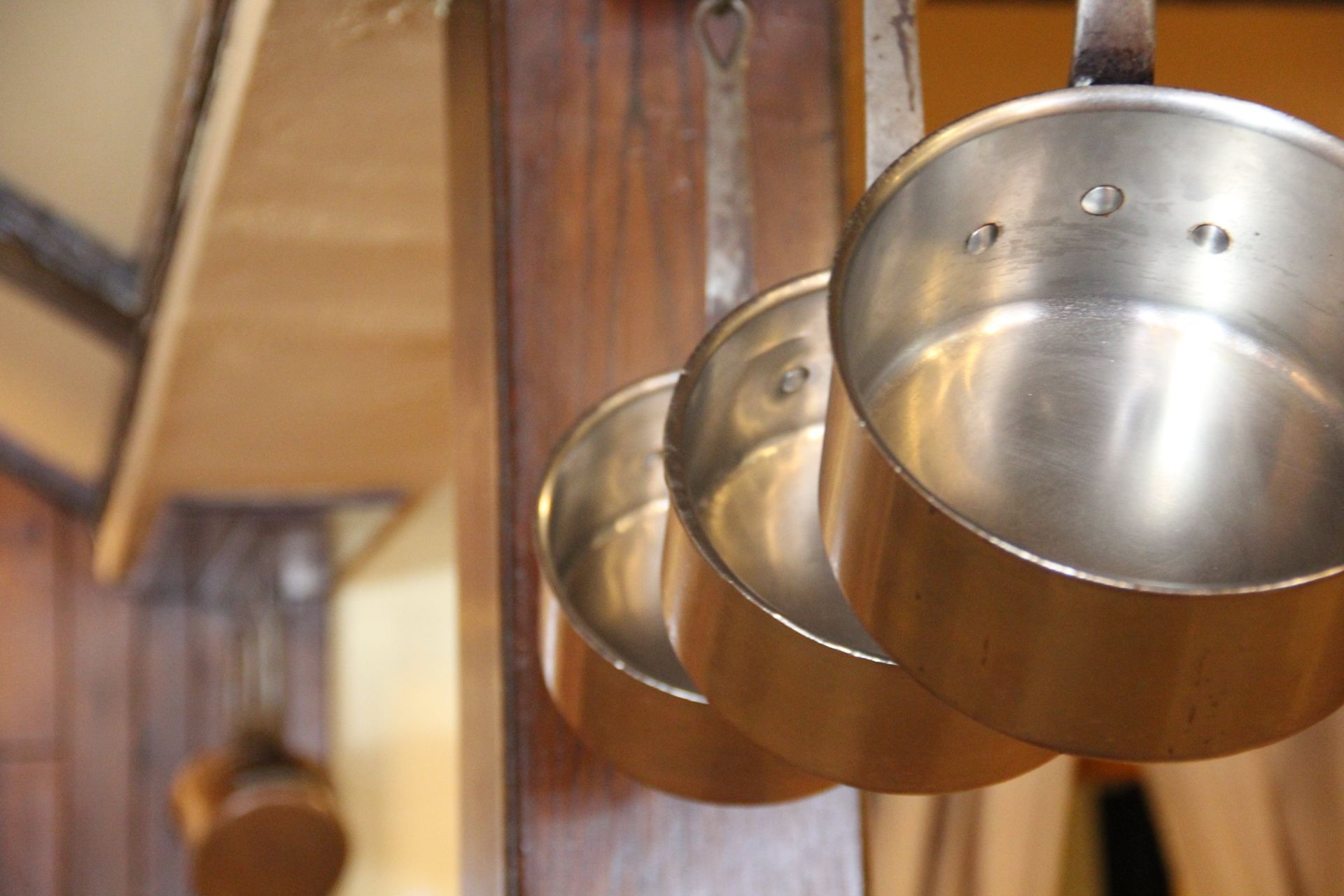 Three pots and pans are hanging on a wooden wall.