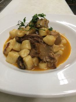 A white plate topped with gnocchi and meat in a sauce.