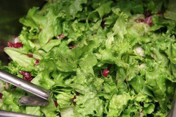 A close up of a salad in a bowl with tongs.