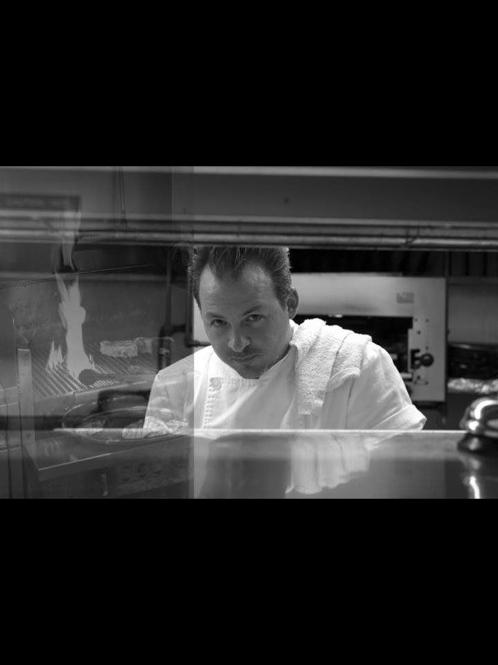 A man in a chef 's uniform is looking through a glass door in a kitchen.