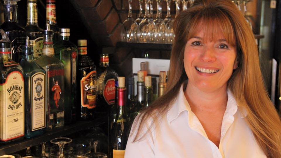 A woman is standing in front of a bar filled with bottles of alcohol including bombay sapphire