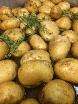 A pile of potatoes sitting in a pot of water with thyme.