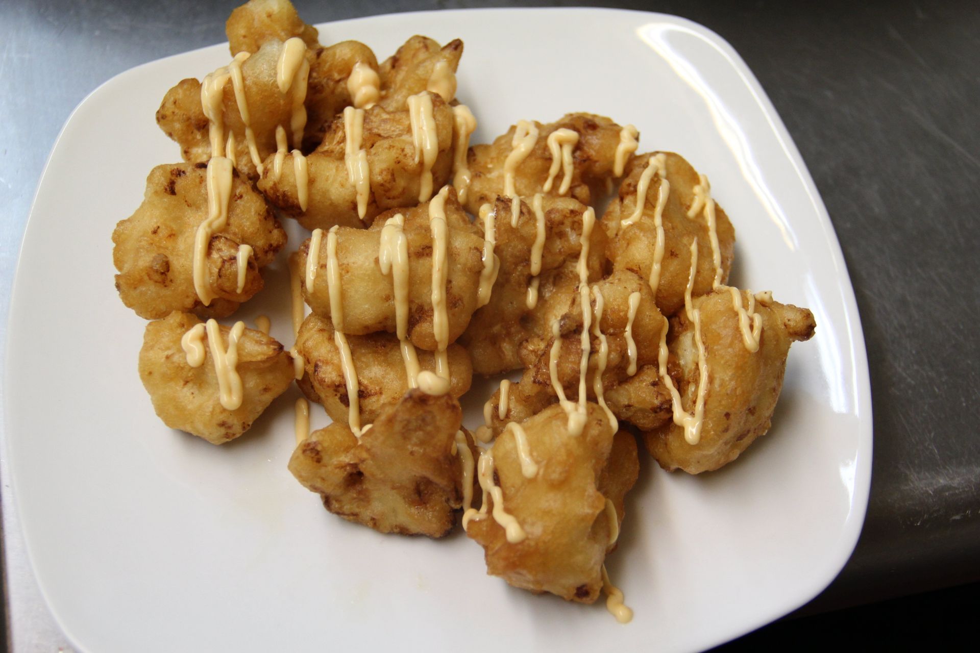 A white plate topped with fried food with mayonnaise on it