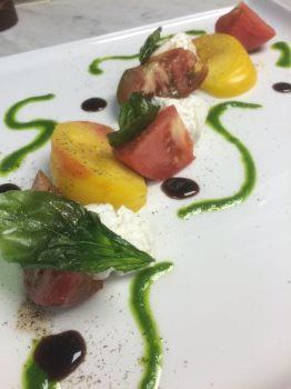 A close up of a plate of food with tomatoes and basil on a table.
