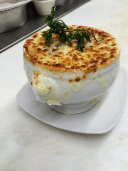 A bowl of french onion soup on a plate on a table.