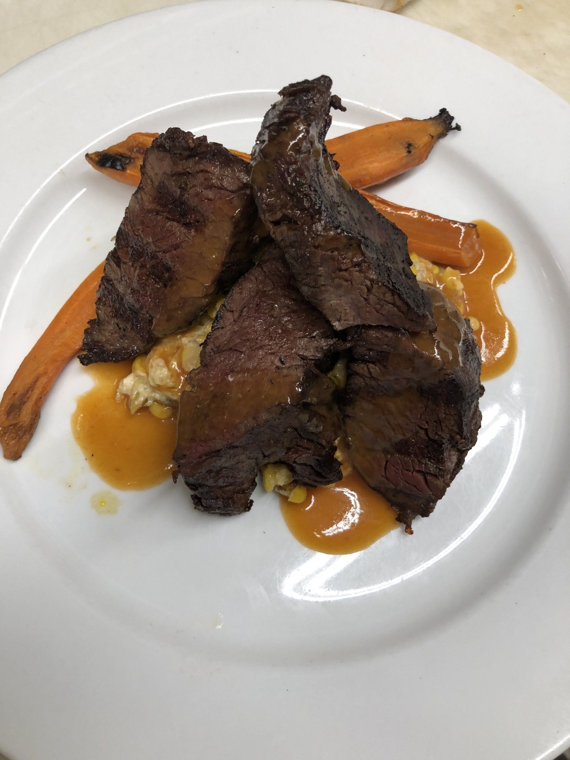 A white plate topped with meat and carrots on a table