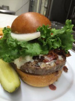 A hamburger with lettuce , bacon , cheese , onions and pickles on a white plate.