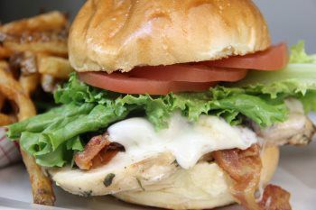 A close up of a chicken sandwich with lettuce , tomato , bacon and cheese on a bun.