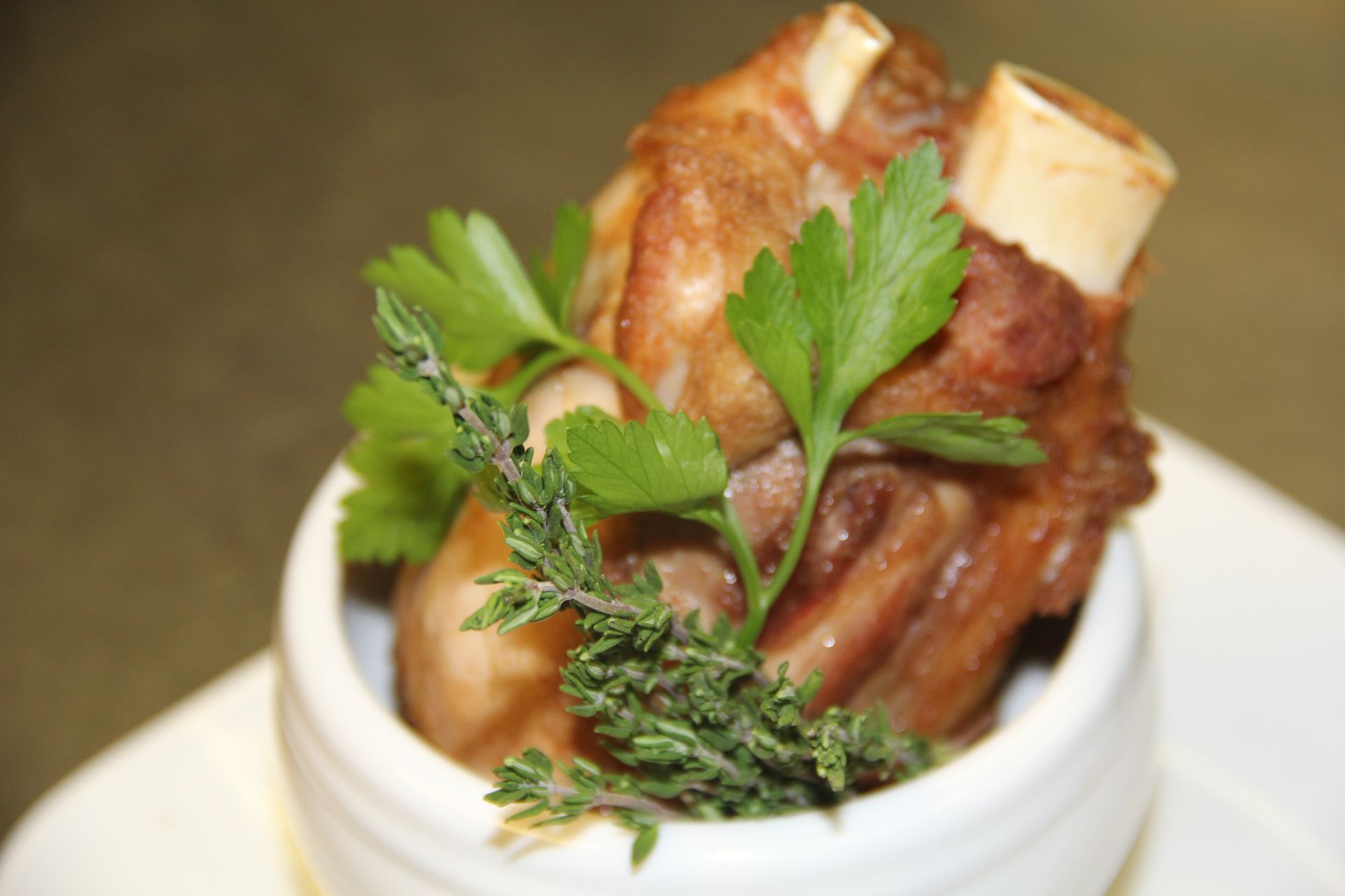 A white bowl filled with meat and parsley on a plate.