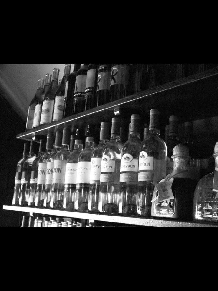 Several bottles of alcohol are lined up on a shelf