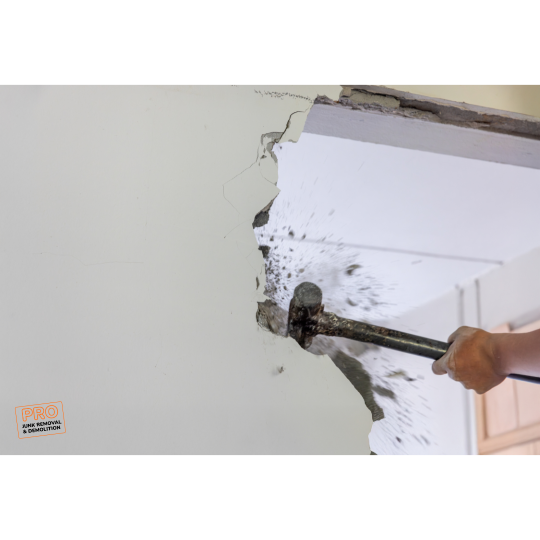 Person using a sledgehammer to demolish a wall, creating debris.