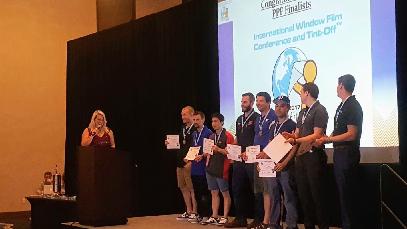 Woman at podium presenting awards to group of men at window film conference.