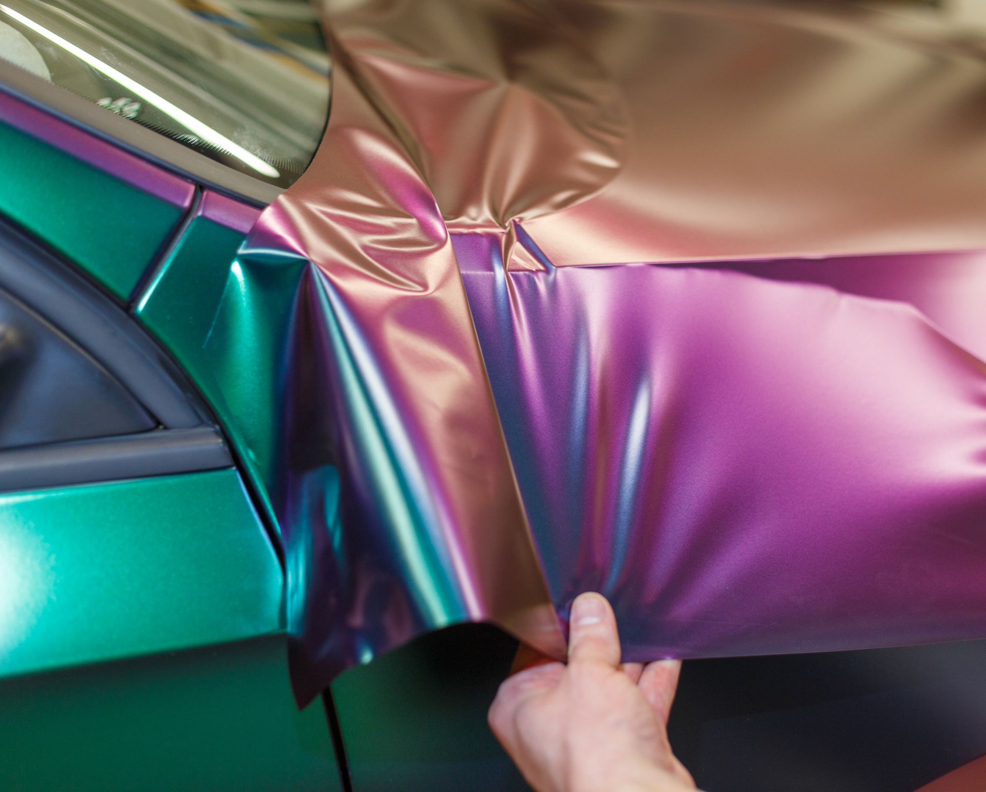 Hand applying iridescent wrap to a green car door.