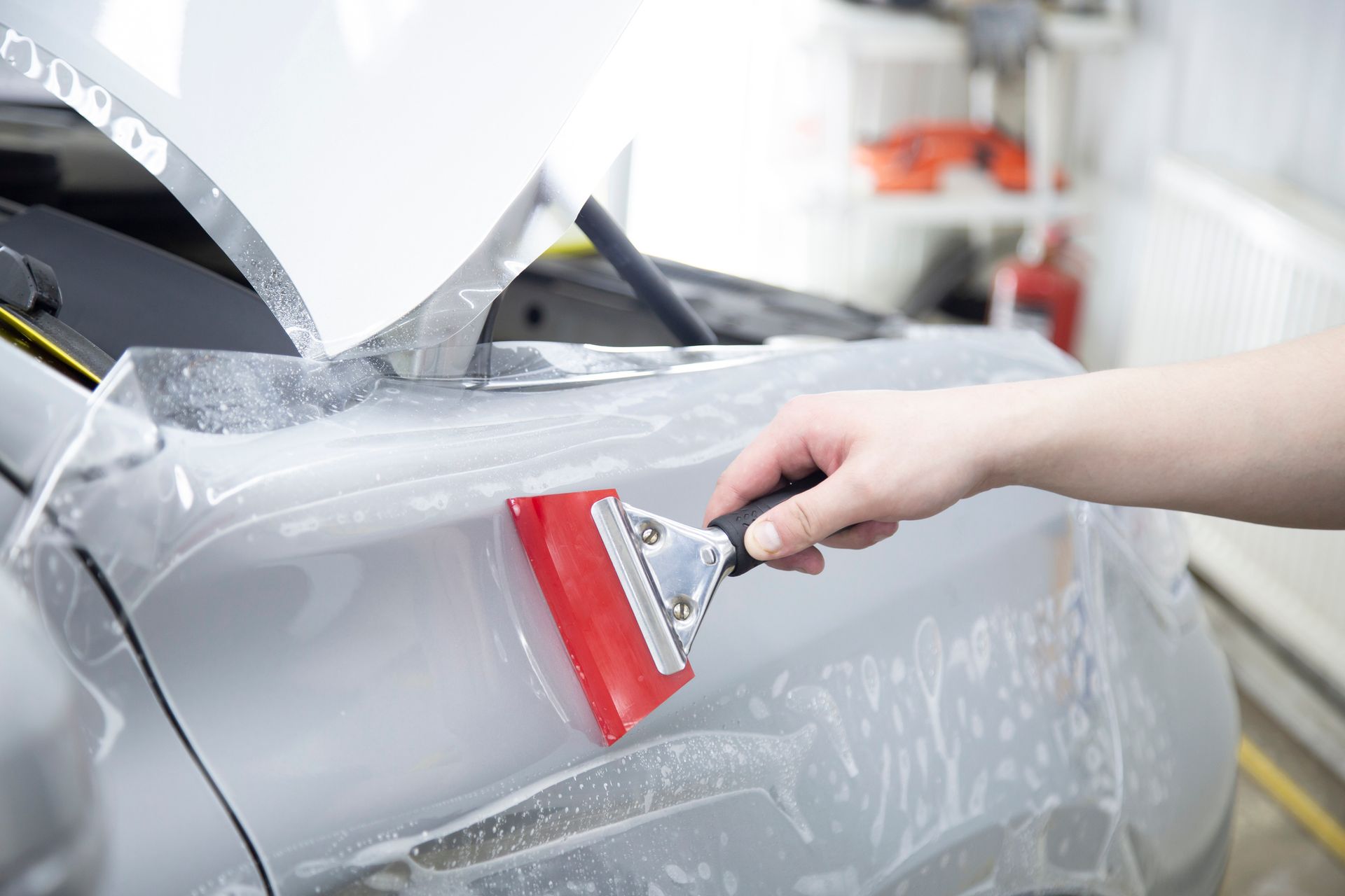 Person applying film to a car door with a red squeegee in a garage.