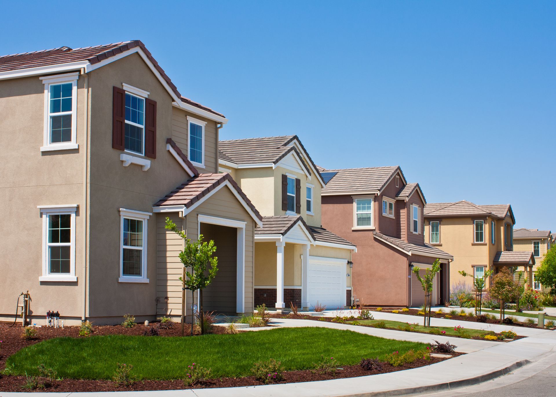 Row of multi-colored houses with front yards, under a clear blue sky.