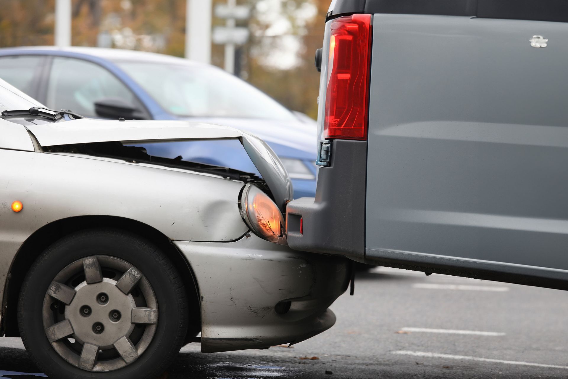 Car accident scene: A silver car has front-end damage, struck by a gray van. A blue car is also visible.