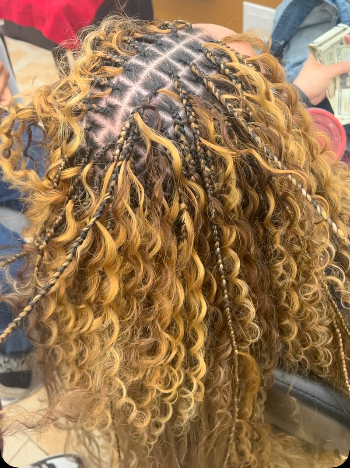 A woman with curly hair is getting her hair braided.