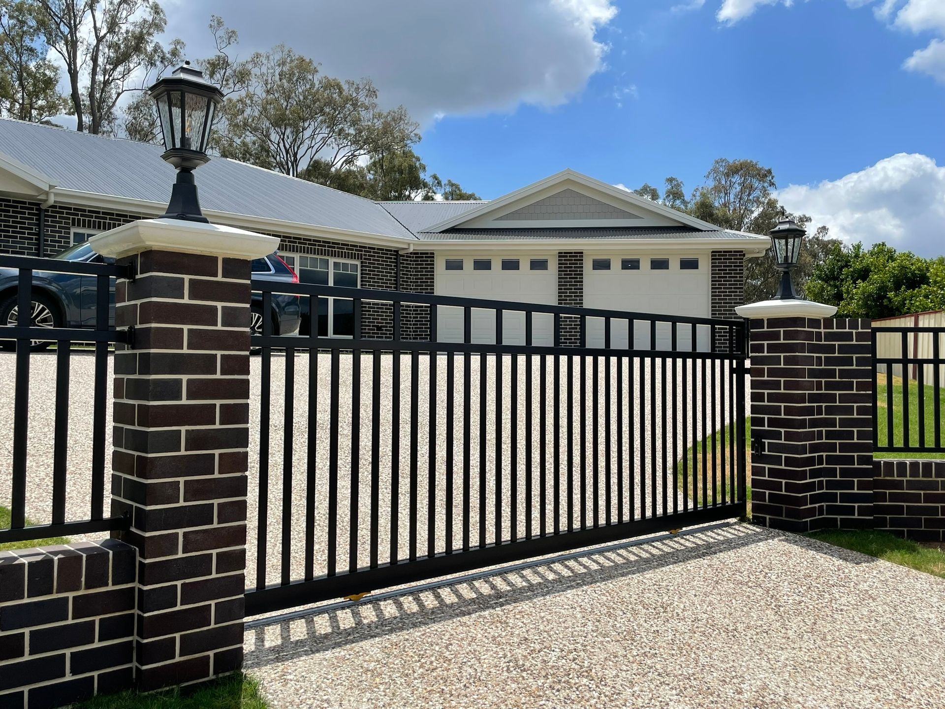 A black and white fence is surrounding a driveway in front of a house.