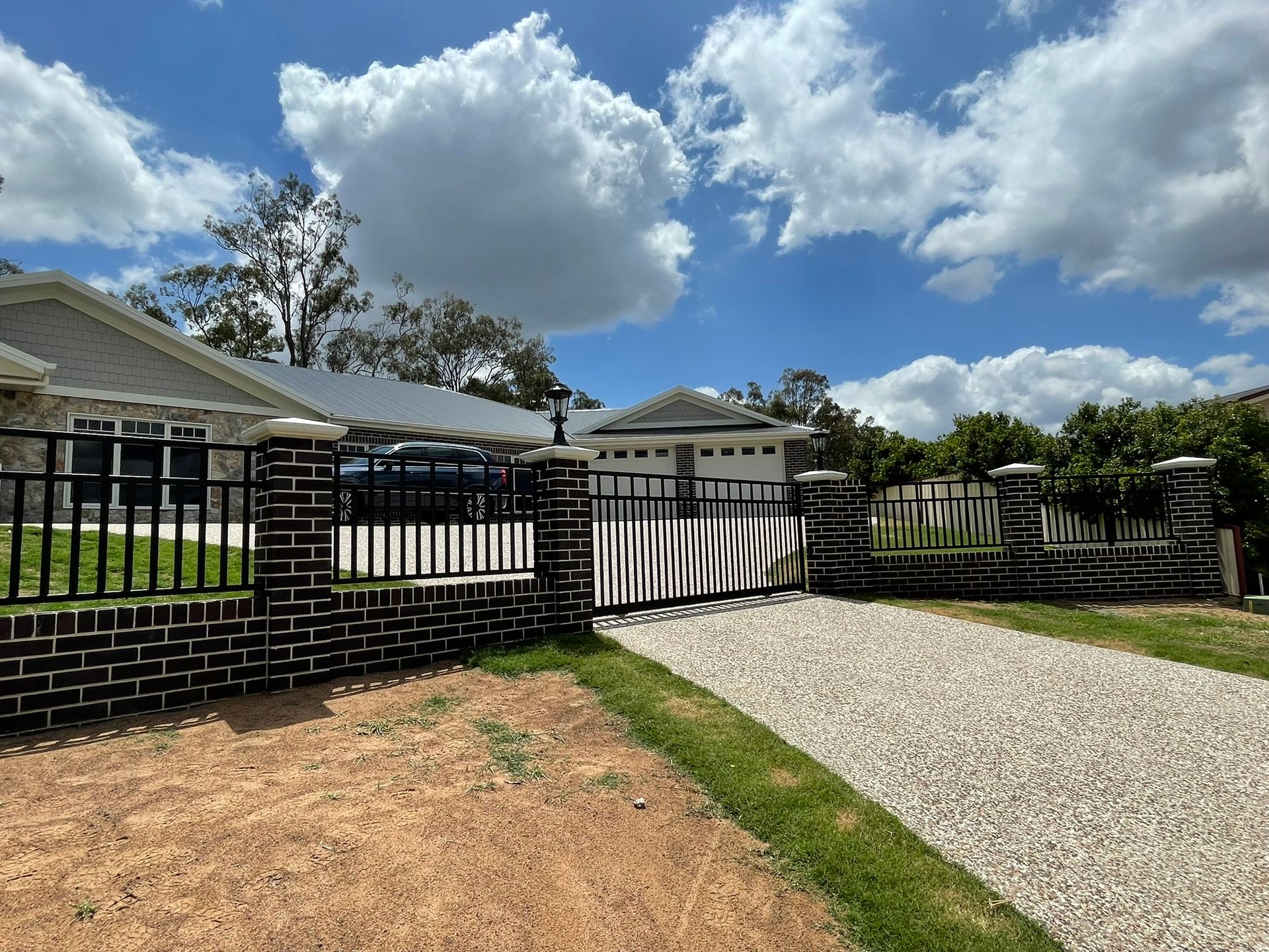 A brick fence surrounds a gravel driveway leading to a house.