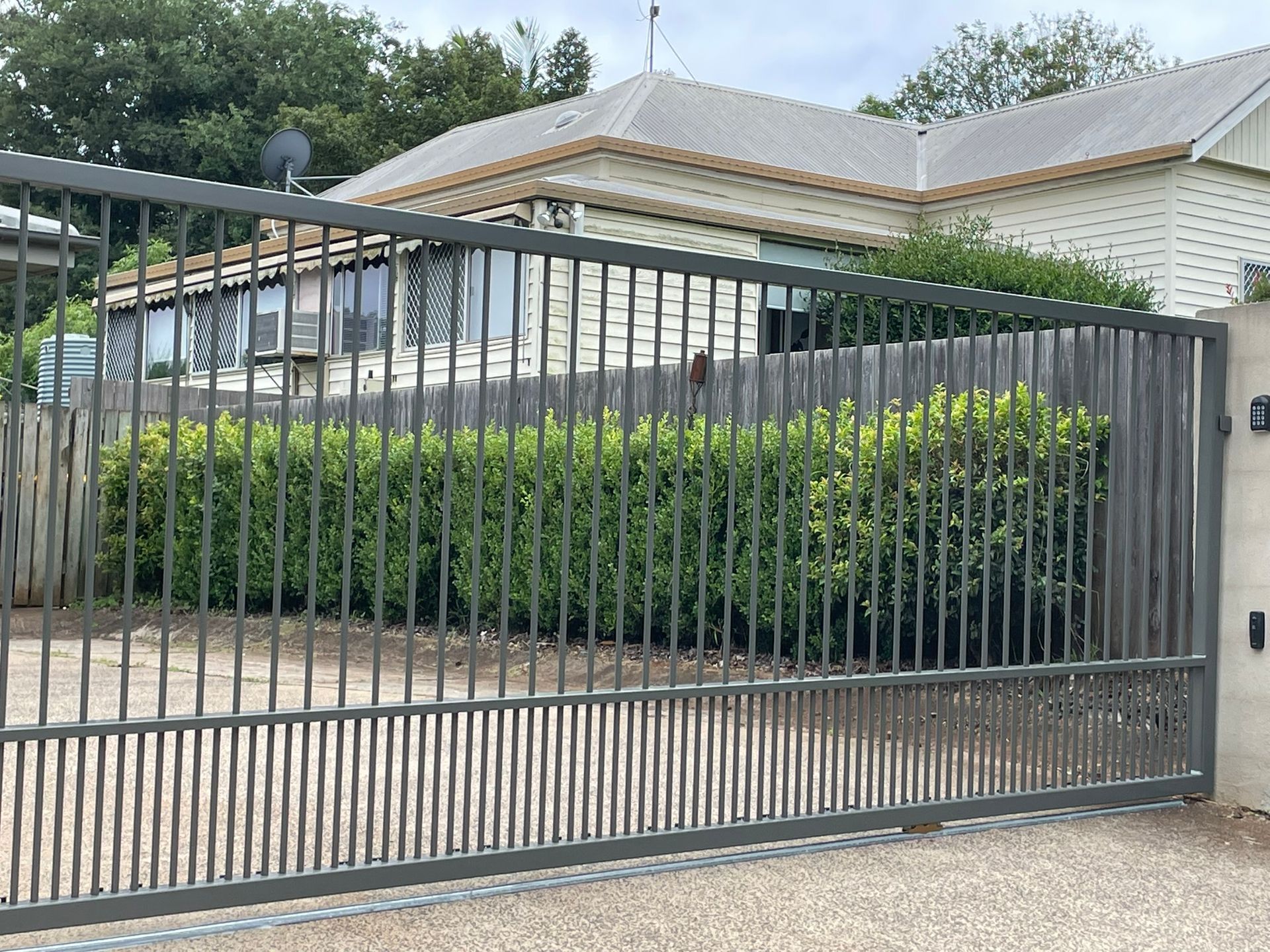 A sliding gate is open to a driveway in front of a house.