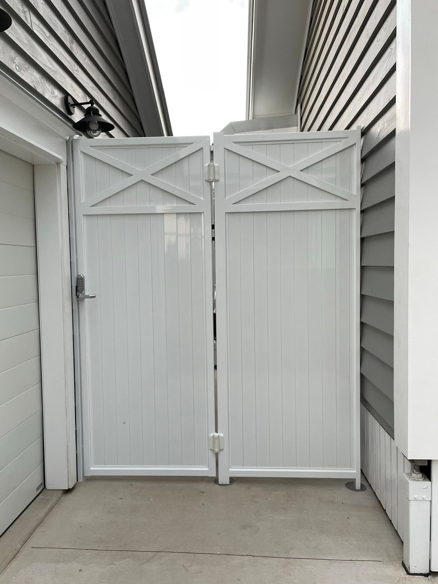 A white gate is between a garage and a house.